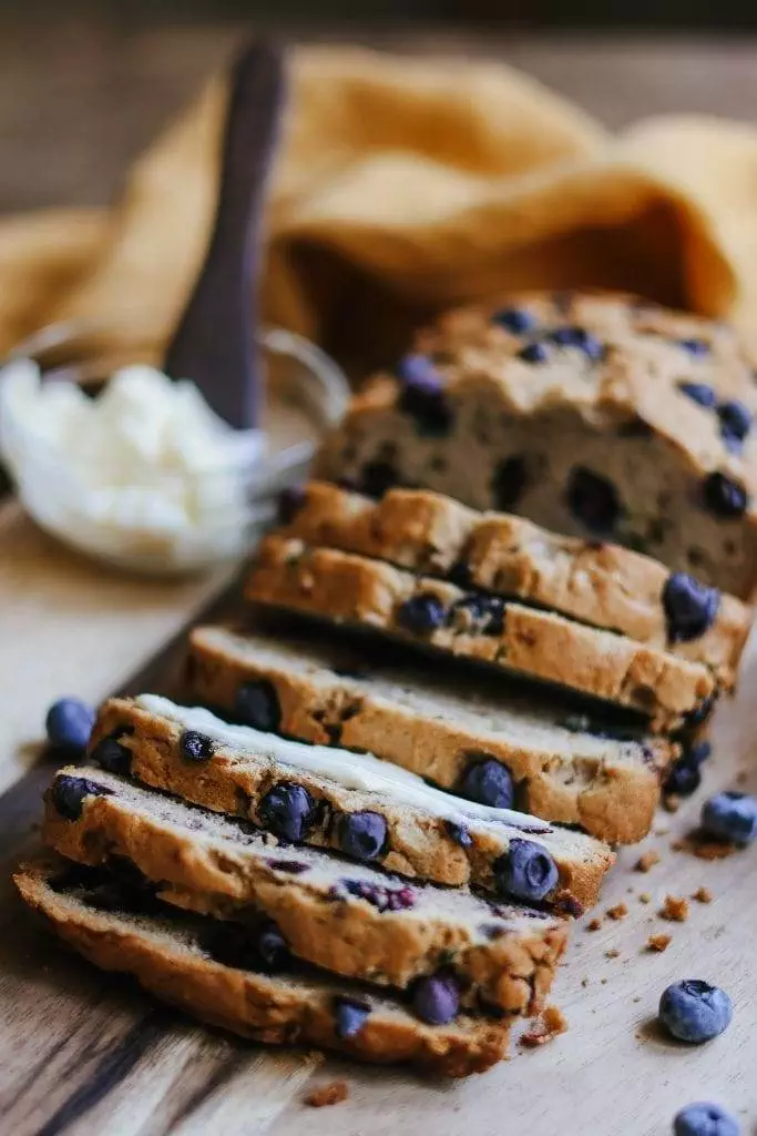 A close-up of zucchini blueberry bread with a slice cut, showing blueberries and zucchini inside.