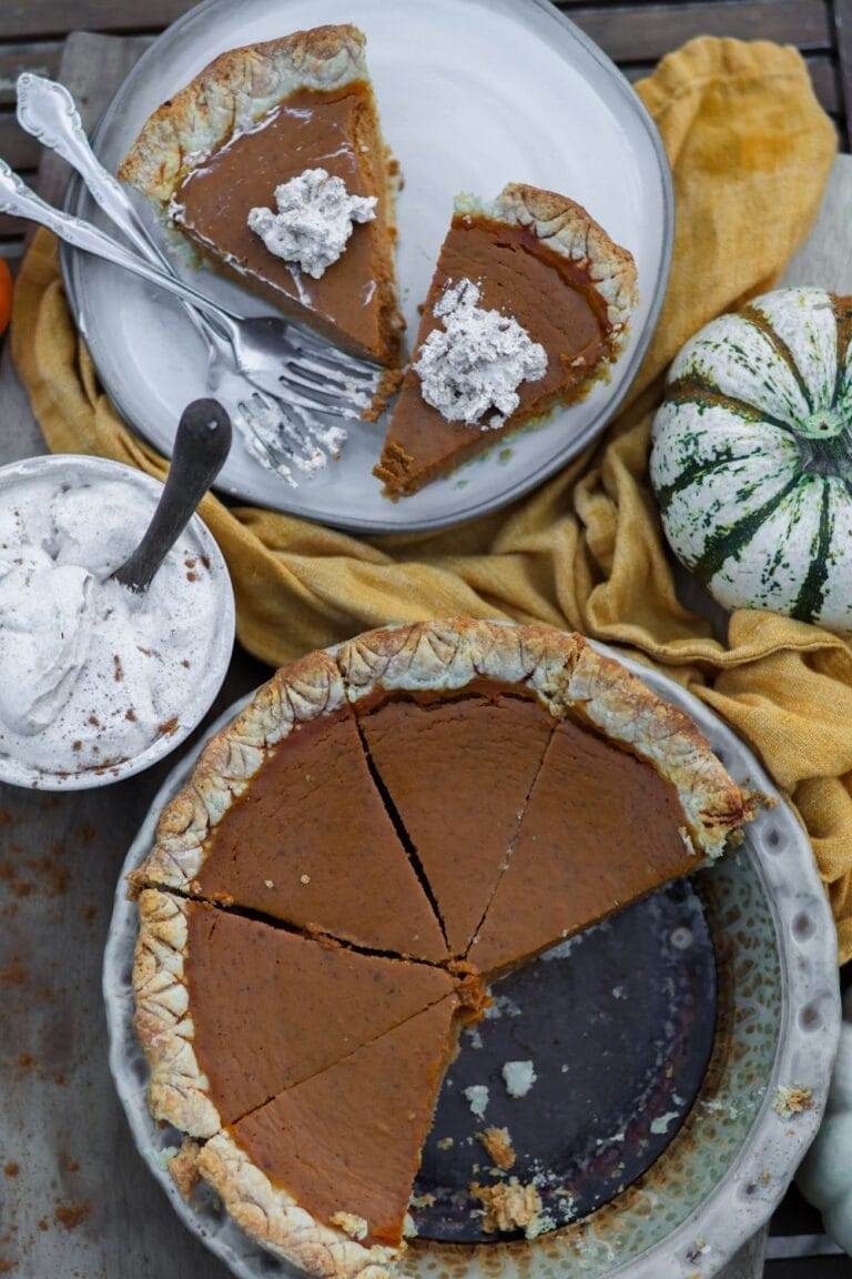 A pumpkin pie in a ceramic dish with two pieces on a plate.