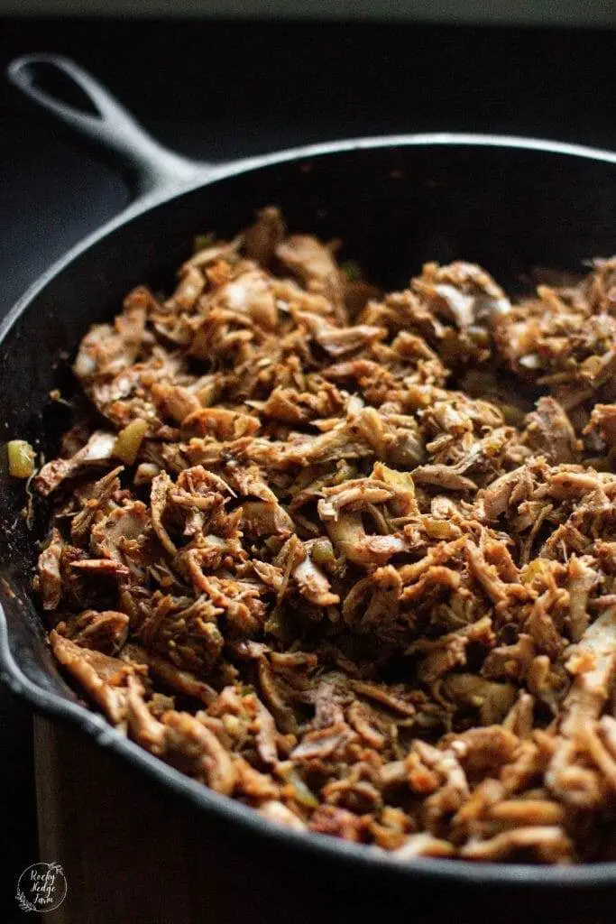 A close-up shot of shredded chicken taco meat cooking in a cast iron skillet, with a golden-brown crust and flavorful spices.