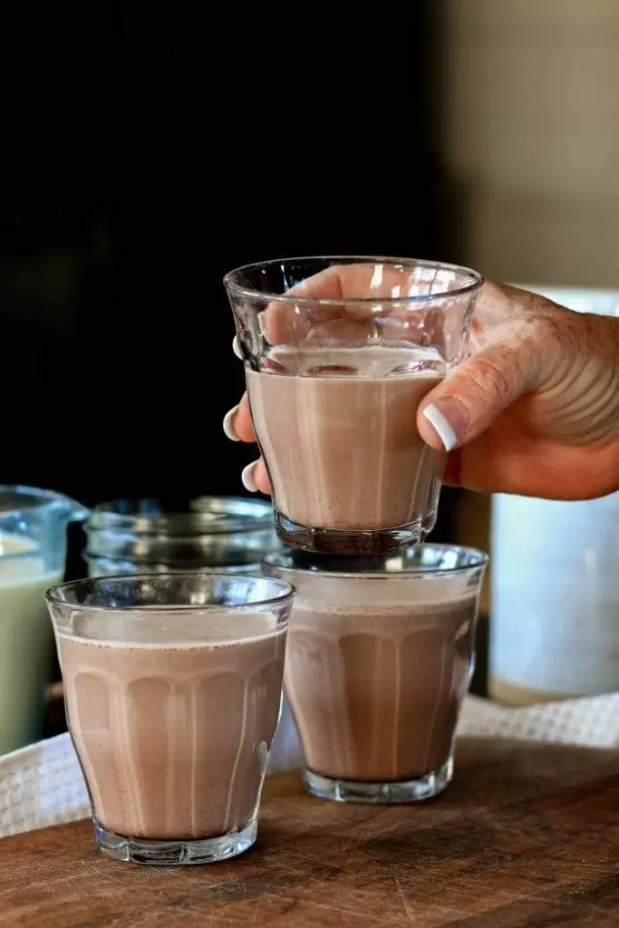 a hand holding a glass of homemade chocolate milk made with cocoa powder