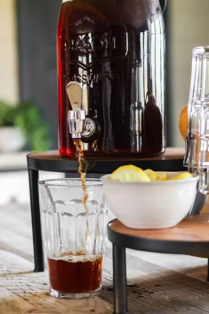 A pitcher of iced tea on a table. The tea is brown color and the pitcher is made of clear glass.