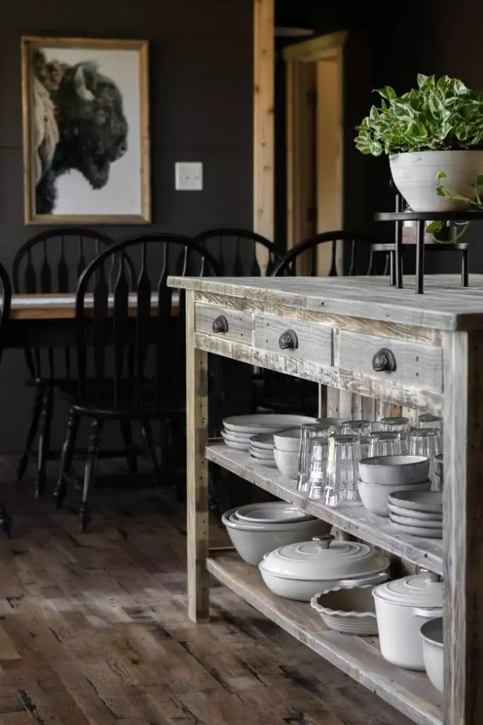 Kitchen island crafted from reclaimed wood, featuring a breakfast nook with two stools and organized storage within the shelves.