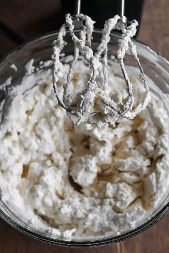 hand mixer and glass bowl with homemade whipped cream that is made with maple syrup and vanilla