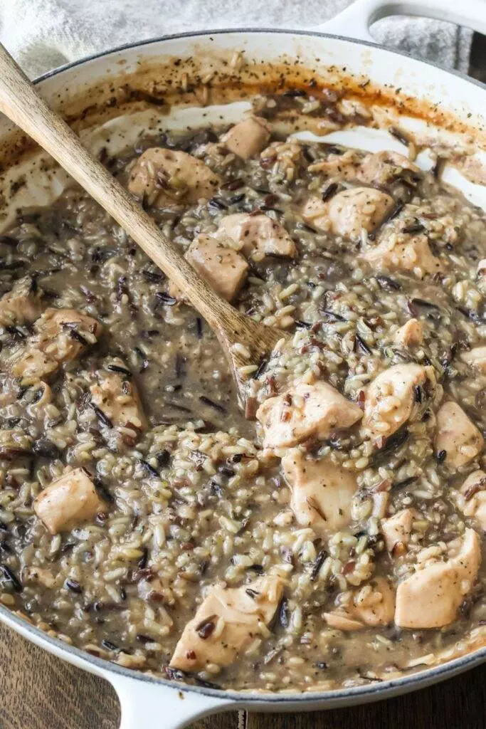 Creamy Chicken and Wild Rice Skillet in a white enamel cast iron pan, with a hearty blend of chicken, wild rice, and savory sauce.