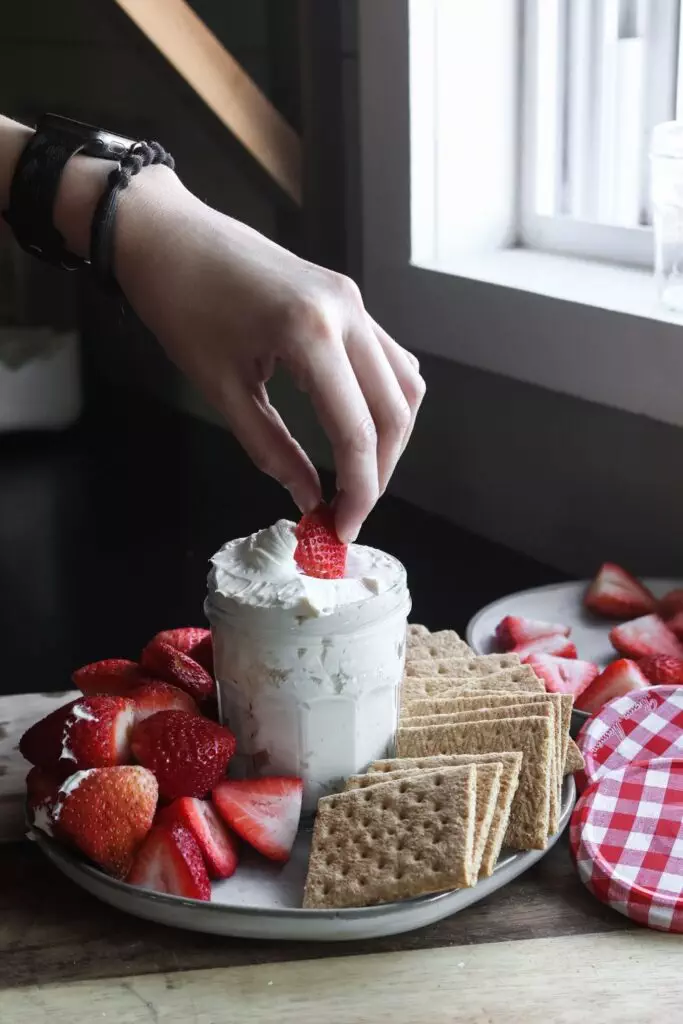 a hand dipping a strawberry into the cheesecake dip