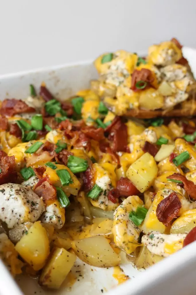 Golden, cheesy Chicken Potato Casserole in a 9x13 casserole dish, topped with crispy bacon, green onions, and melted cheddar cheese, ready to serve.