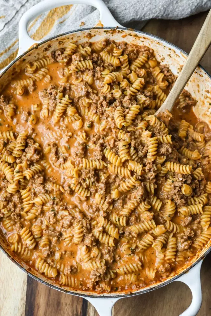 A delicious cheesy ground beef pasta cooked in a cast iron enameled skillet, with gooey melted cheese and tender pasta mixed with savory beef.