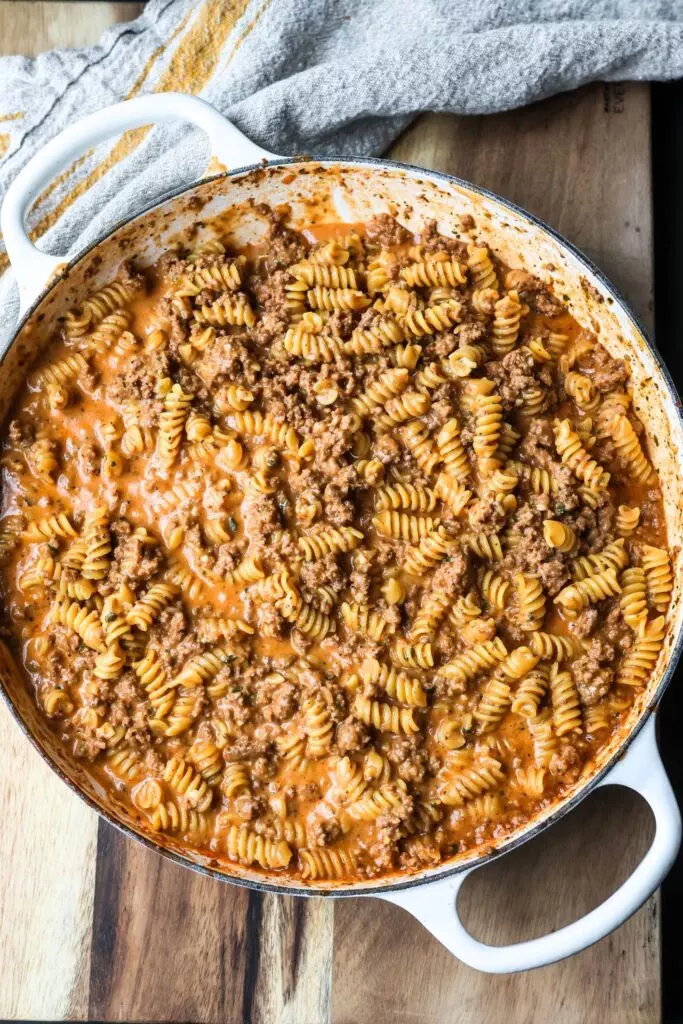 Close-up of cheesy ground beef pasta skillet in a cast iron enameled pan, showcasing the creamy, cheesy sauce and tender pasta.