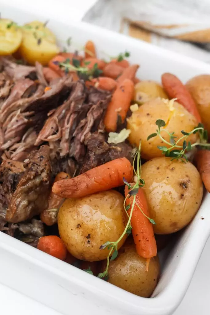 A plate of shredded pot roast alongside hearty potatoes and carrots, all cooked to perfection.