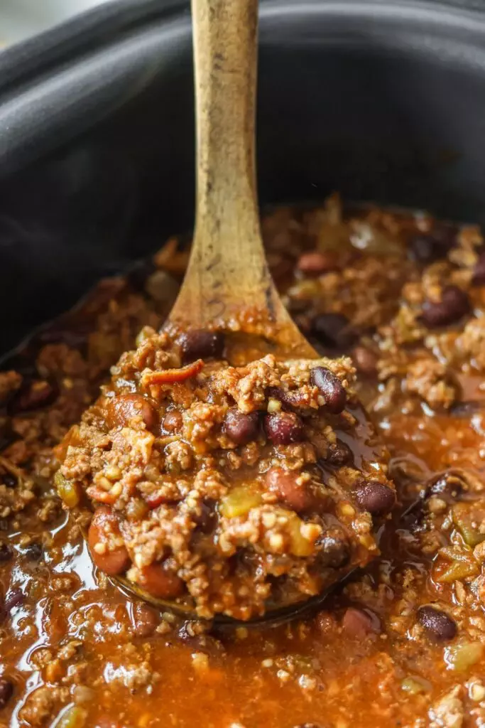 Chili with bacon cooking in a slow cooker, filled with vibrant chili beans and a rich, savory broth.