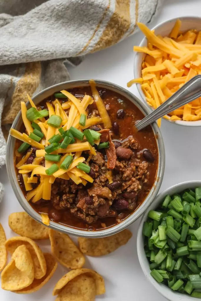 Hearty serving of chili with bacon in a bowl, garnished with green onions and shredded cheese